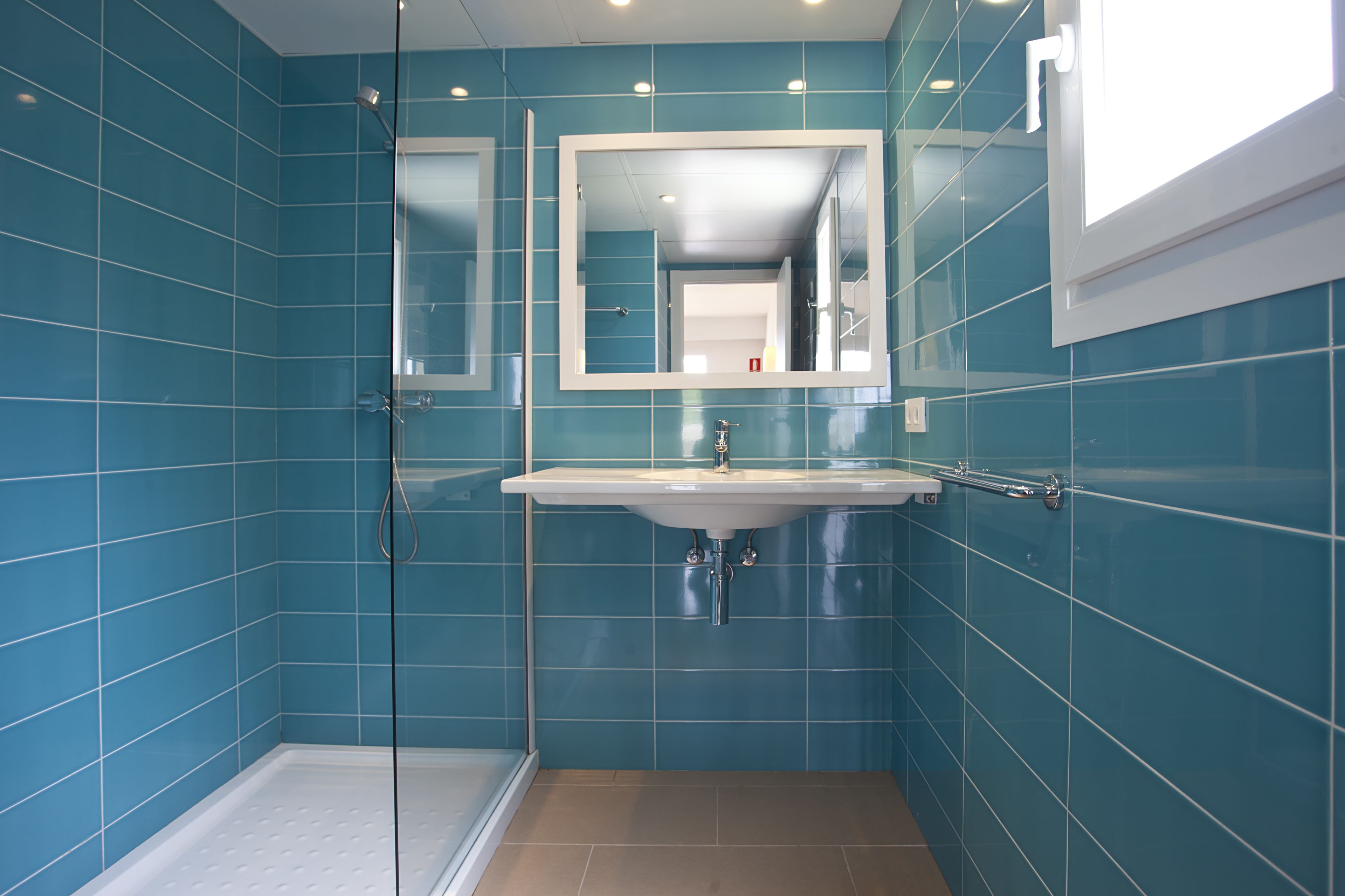 A bathroom with blue tiles, a glass shower enclosure, a sink, and a mirror.