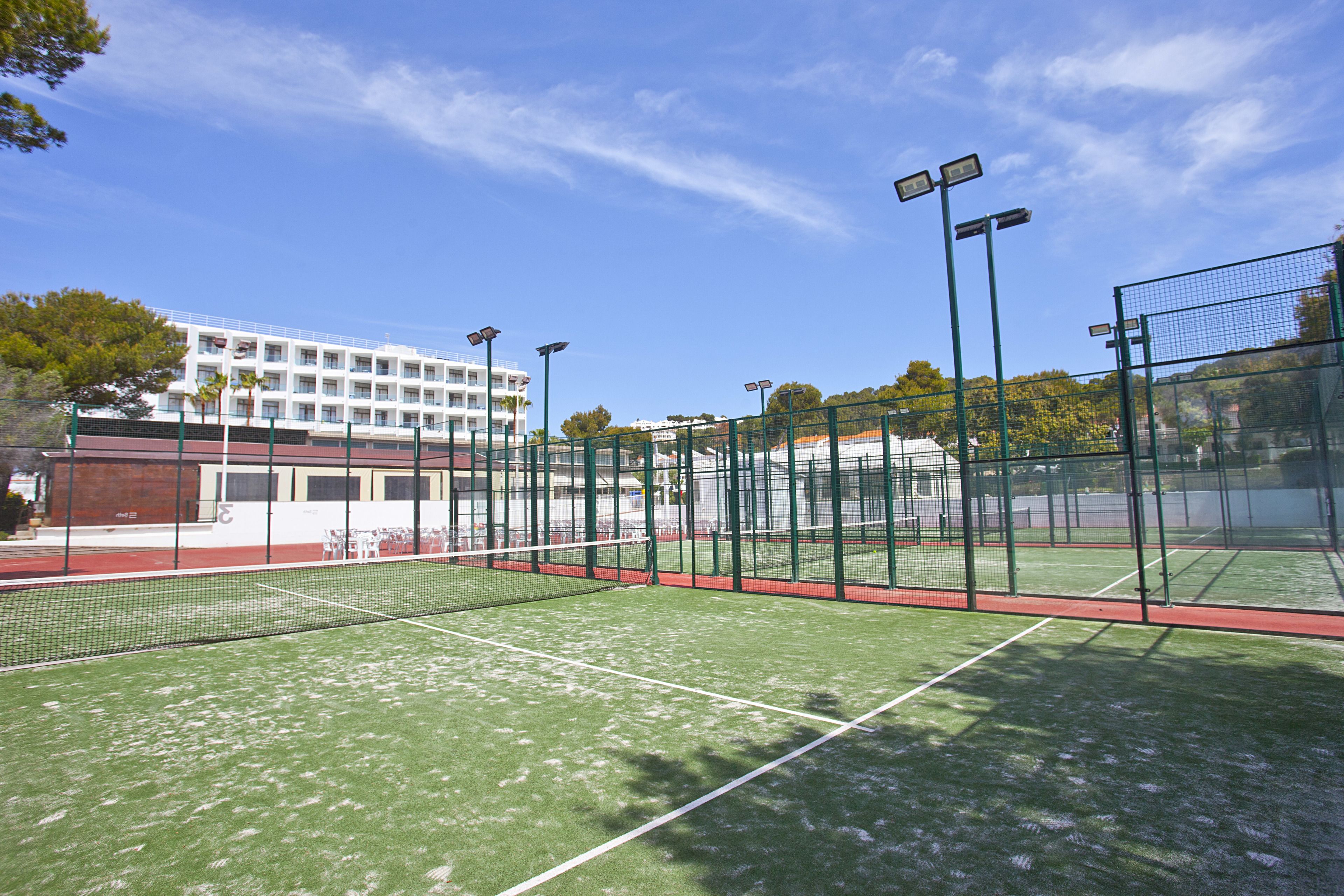 Un court de tennis extérieur doté d’une surface en gazon synthétique vert, entouré d’une clôture verte et équipé de projecteurs.