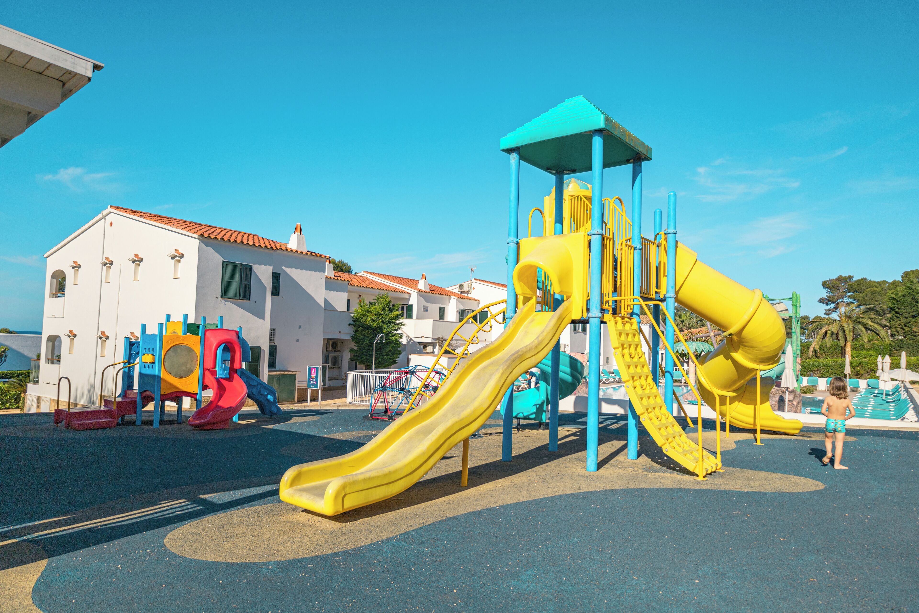 Ein Spielplatz mit mehreren Rutschen und Klettergerüsten neben einem weißen Gebäude mit rotem Ziegeldach.