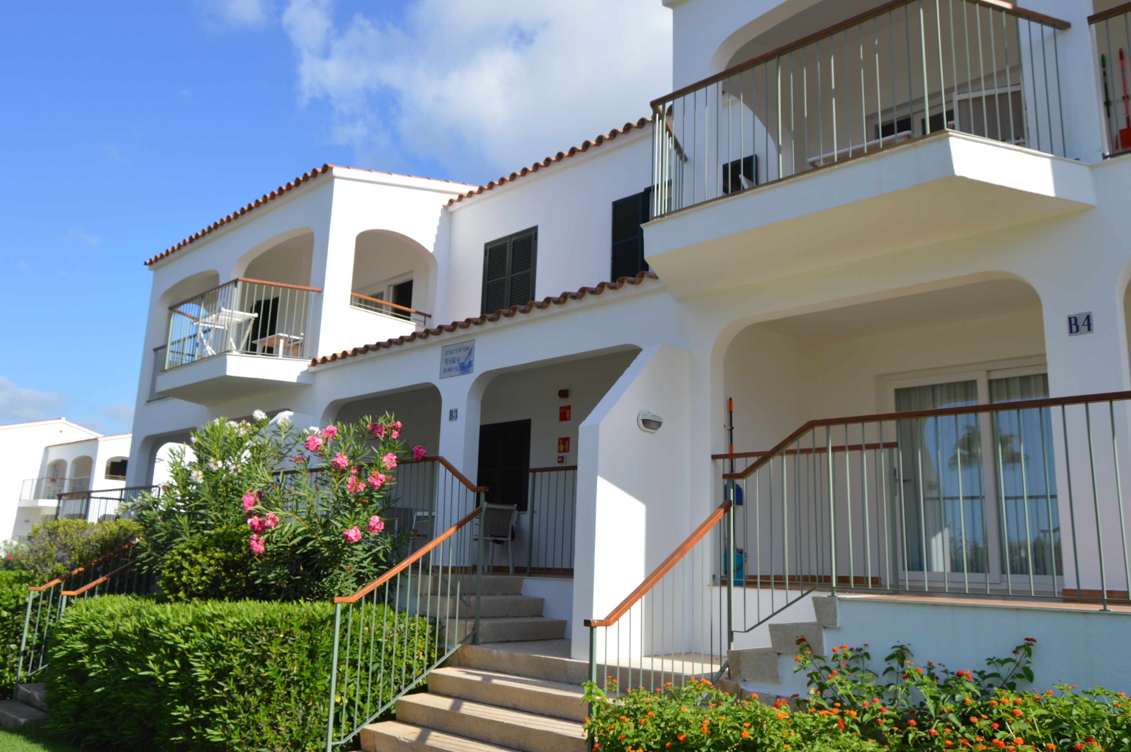 A two-story building with balconies, a staircase, and a sign indicating a rental price.
