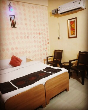A hotel room with a bed, two chairs, an air conditioner, and a wall-mounted picture. - Hotel Blue Star By Amazone Holidays (Haldwani)