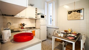 A modern kitchen with white cabinets, a red baking dish, a gas stove, and a microwave. - Wanderlust, 3 Bedroom Air Conditioned Apartment in Trastevere (Rome)