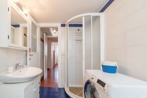 A bathroom with a sink, mirror, shower, and a washing machine.