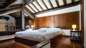 A bedroom with a wooden ceiling, a bed with a patterned bedspread, two bedside tables with lamps, and a wooden bench. - Cozy Apartment in via dei Cappellari, Campo de' Fiori (Rome)