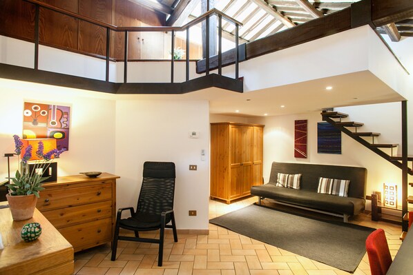 A spacious living area with a high ceiling, wooden staircase, and a sofa with cushions.