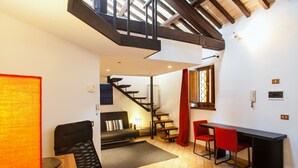 A modern living space with a staircase, a sofa, a dining table with chairs, and a red curtain. - Cozy Apartment in via dei Cappellari, Campo de' Fiori (Rome)
