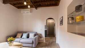 A living room with a grey sofa, a round wooden table with a vase of flowers, and a bookshelf with books and decorative items. - Cozy Apartment in via Degli Spagnoli, Pantheon (Rome)