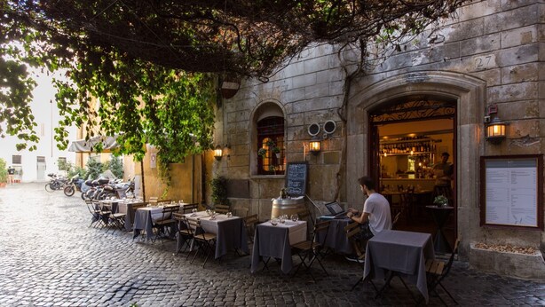 An outdoor café with tables and chairs, a cobblestone street, and a building with a sign. - Cozy Apartment in via Degli Spagnoli, Pantheon (Rome)