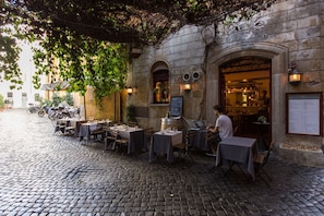 An outdoor café with tables and chairs, a cobblestone street, and a building with a sign.