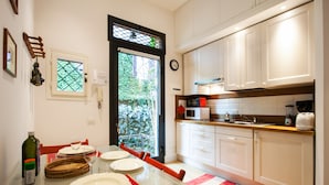 A modern kitchen with white cabinets, a microwave, and a coffee maker. There is a dining table with plates and a red placemat. - Domus Claudiae (Rome)