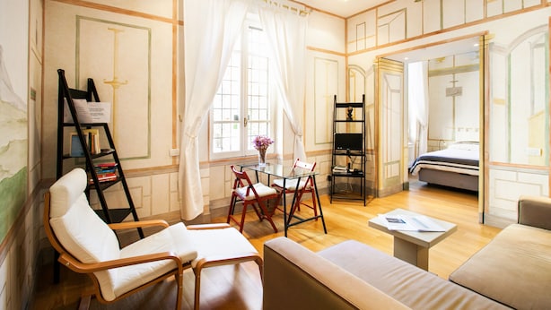 A well-lit room with a sofa, chairs, a small table, and a bookshelf. - Domus Claudiae (Rome)