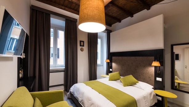 Habitación de hotel con una cama grande, sillones verdes, techo de madera y un televisor en la pared.