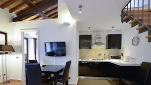 Una cocina moderna con una televisión de pantalla plana, una zona de comedor con mesa y sillas, y una escalera.