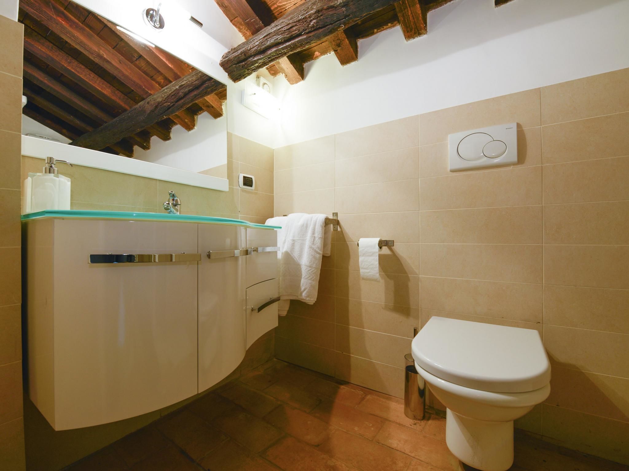 Un baño con inodoro blanco, lavamanos de cristal y baldosas color beige.