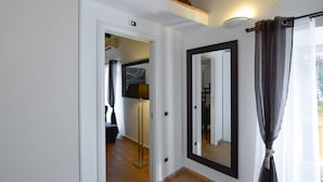 Un pasillo con un espejo, una puerta que da a una habitación y una ventana con cortinas.