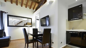 Una sala moderna con comedor, televisor montado en la pared y cocina equipada con pileta y estufa.