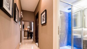 A hallway with framed pictures, a dining area with a table and chairs, and a modern bathroom with a glass shower enclosure. - The Brunetti - Luxury Serviced Apartment (Rome)