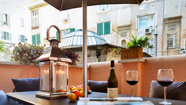A table with a laptop, wine bottle, and glasses, surrounded by cushions and a lantern. - The Brunetti - Luxury Serviced Apartment (Rome)