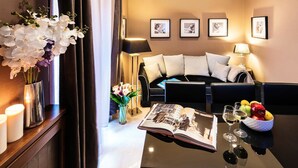 A modern hotel room with a black leather sofa, a coffee table with a book and glasses, a vase with white flowers, and framed pictures on the wall. - The Brunetti - Luxury Serviced Apartment (Rome)