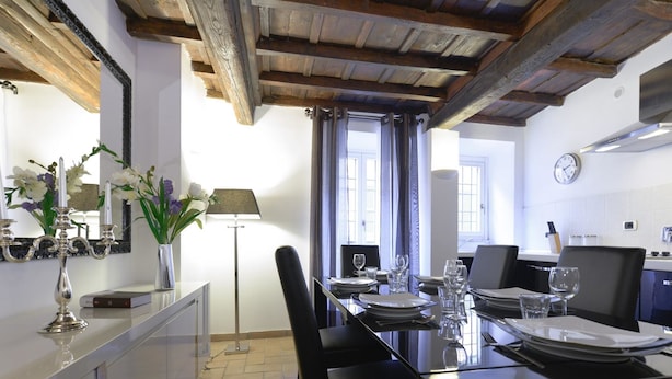 Un comedor con techo de madera, una mesa de comedor lista con platos, vasos y cubiertos, y un jarrón con flores a un lado.