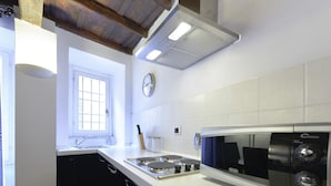 Una cocina moderna con encimeras blancas, una estufa de acero inoxidable, un microondas y un ventanal con persianas.
