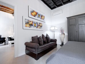 Un dormitorio moderno con una cama grande, un sofá marrón oscuro, dos cuadros abstractos, una lámpara de pie y un armario gris.