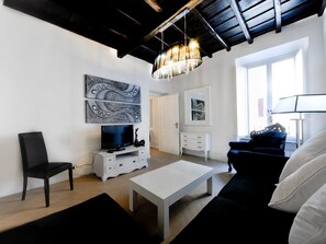 Una sala de estar moderna con un televisor de pantalla plana, muebles blancos y obras de arte en las paredes.