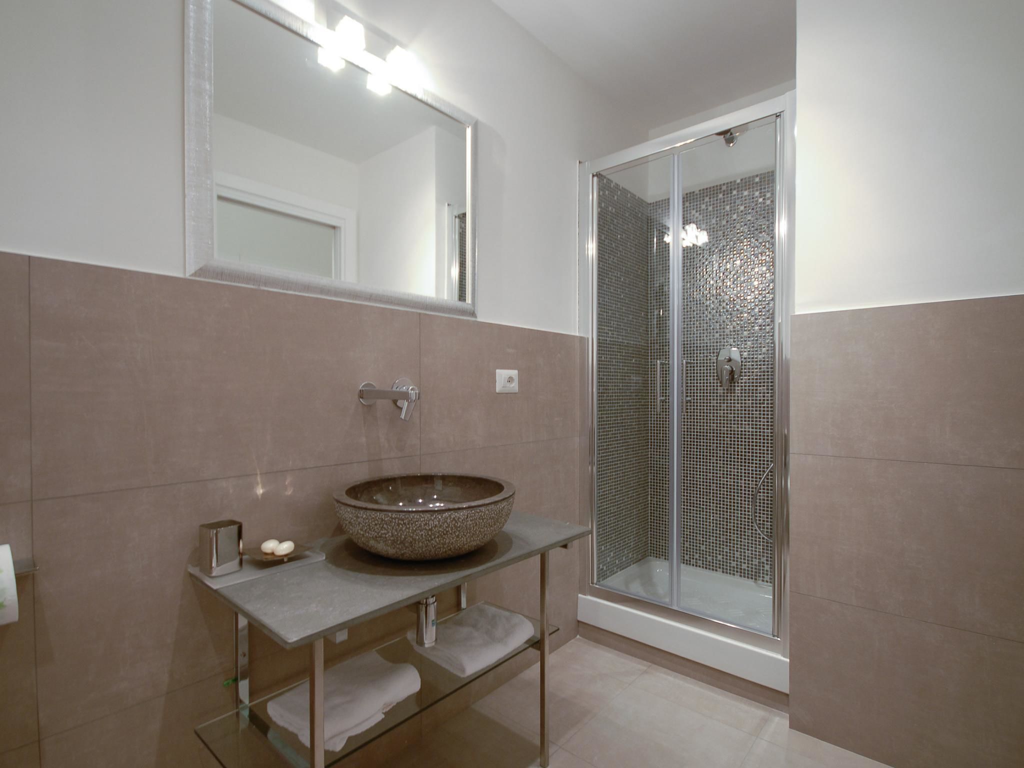 Une salle de bain moderne dotée d’une douche à parois de verre, d’un lavabo rond et d’un miroir avec éclairage intégré.
