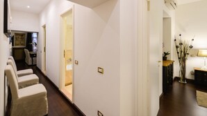 Un pasillo con una zona de estar, una puerta que da a un baño y una mesita con lámpara y plantas decorativas.