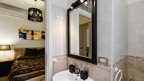A modern bathroom with a white sink, a mirror with a black frame, and a shower area. - Spagna Apartment (Rome)