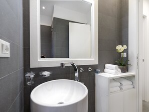 A modern bathroom with a white sink, a large mirror, and a small potted orchid. - Popolo Apartment (Rome)