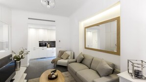 Un salon moderne avec un canapé, une table basse, un téléviseur et une cuisine en arrière-plan.