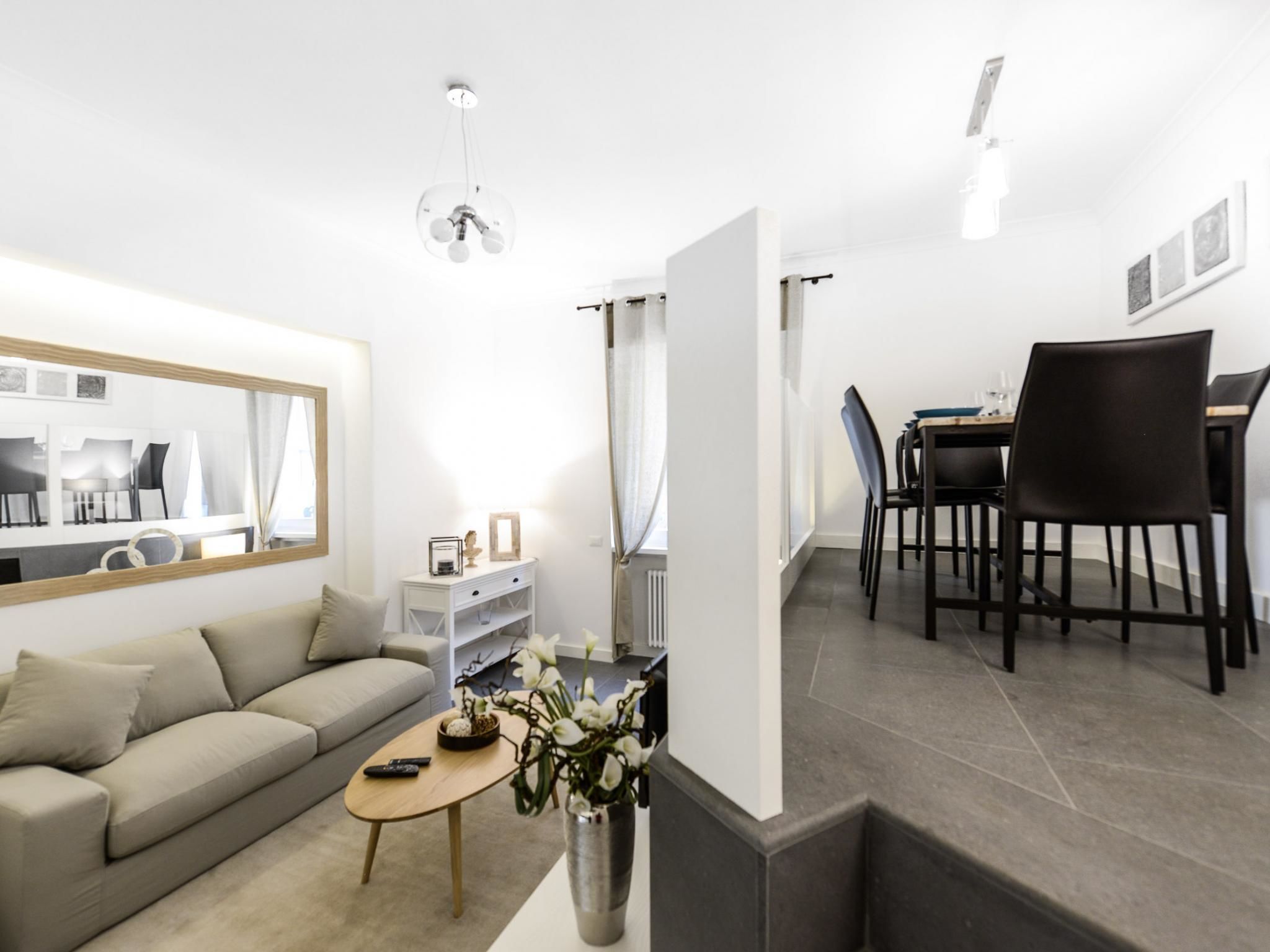 A modern living room with a sofa, coffee table, and a dining area with chairs and a table.