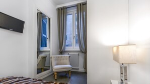 Une chambre d’hôtel avec un lit, une chaise, une fenêtre avec des rideaux, un radiateur et une lampe.
