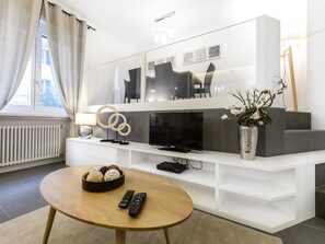 A modern living room with a TV, white entertainment unit, and a round wooden coffee table. - Popolo Apartment (Rome)