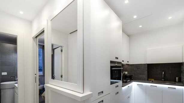 Une cuisine moderne avec des meubles blancs, un four encastré et un grand miroir.