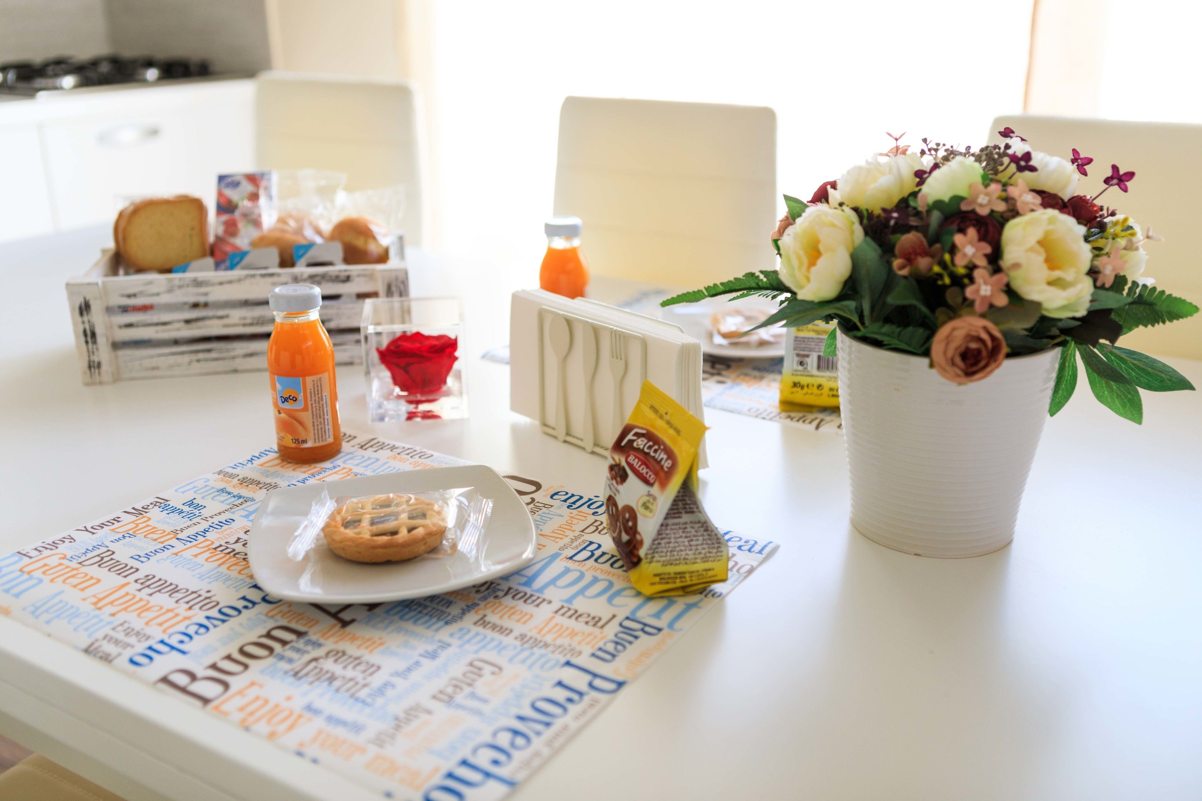 Et morgenbord med en avis, en blomstervase, en tallerken med en croissant, en appelsinjuiceflaske og en kaffepakke.