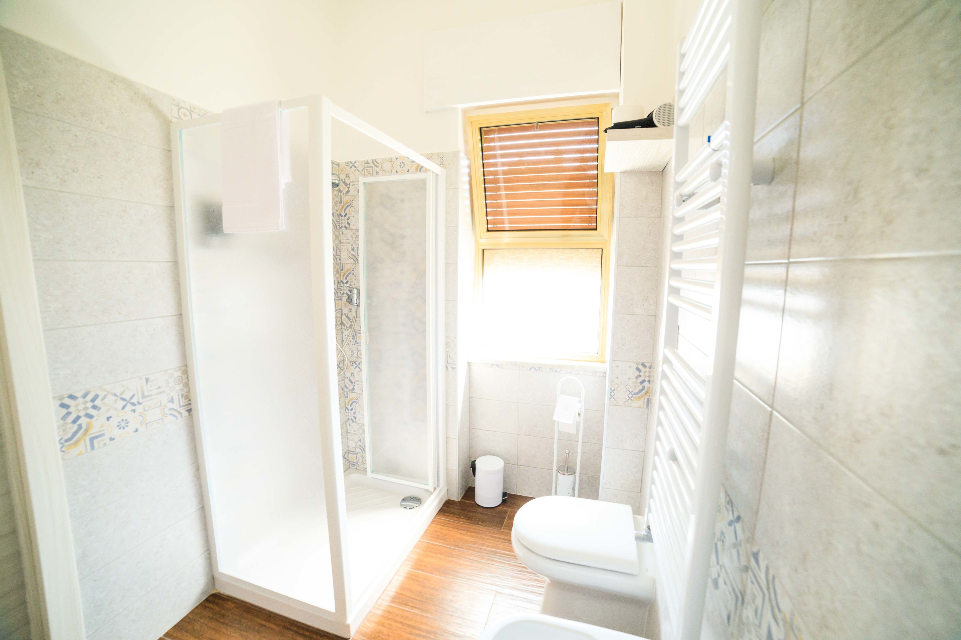 A bathroom with a shower, toilet, and a window.