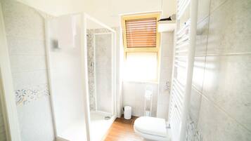 A bathroom with a shower, toilet, and a window.