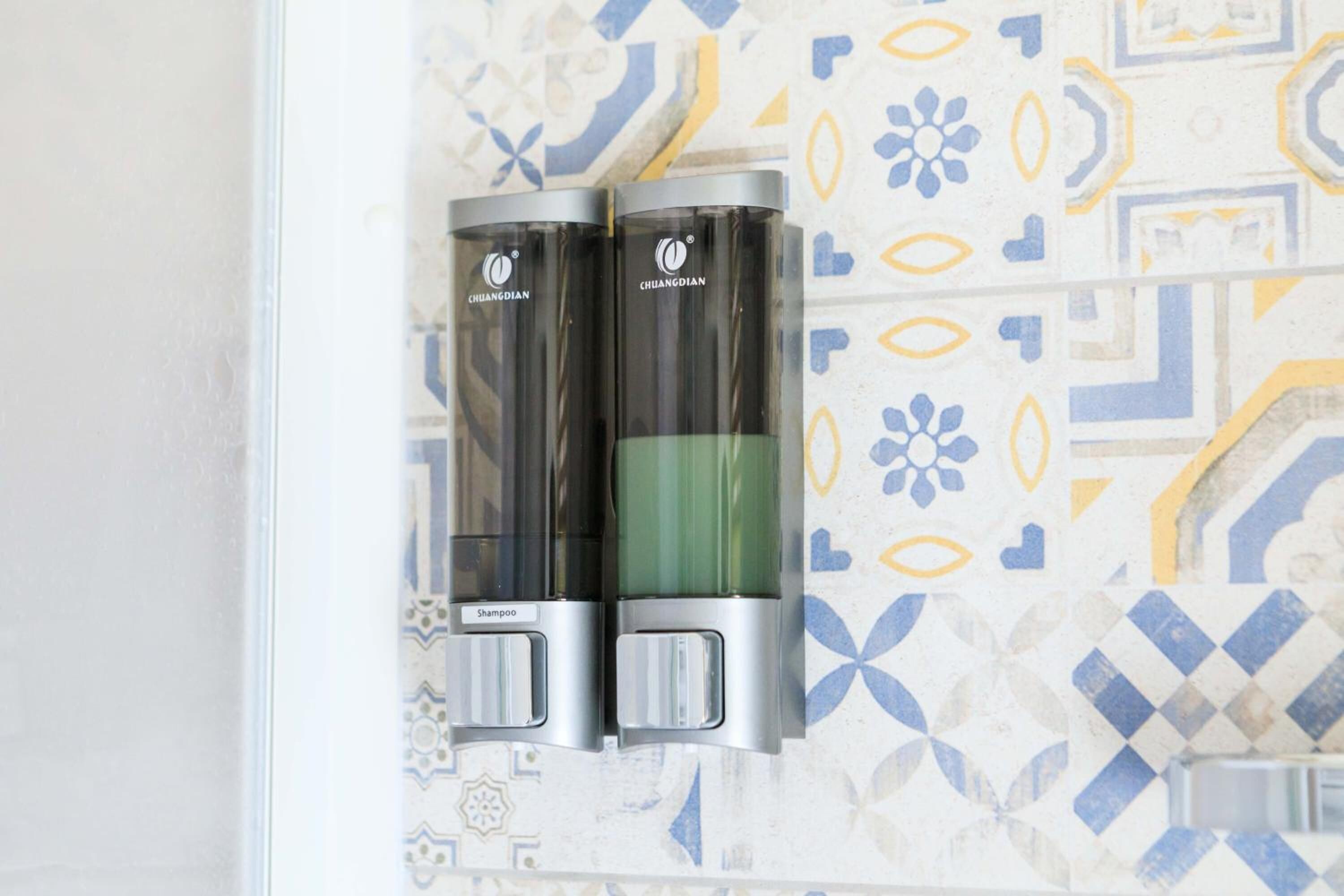Dos dispensadores de champú montados en una pared con un salpicadero de azulejos estampados.