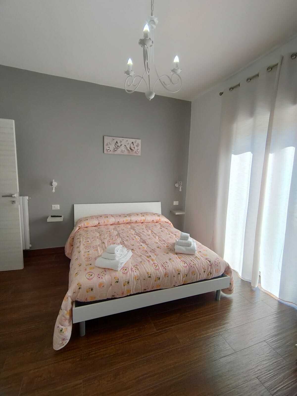 Une chambre à coucher avec un lit, un lustre, une table de chevet, une horloge murale et une fenêtre avec des rideaux.