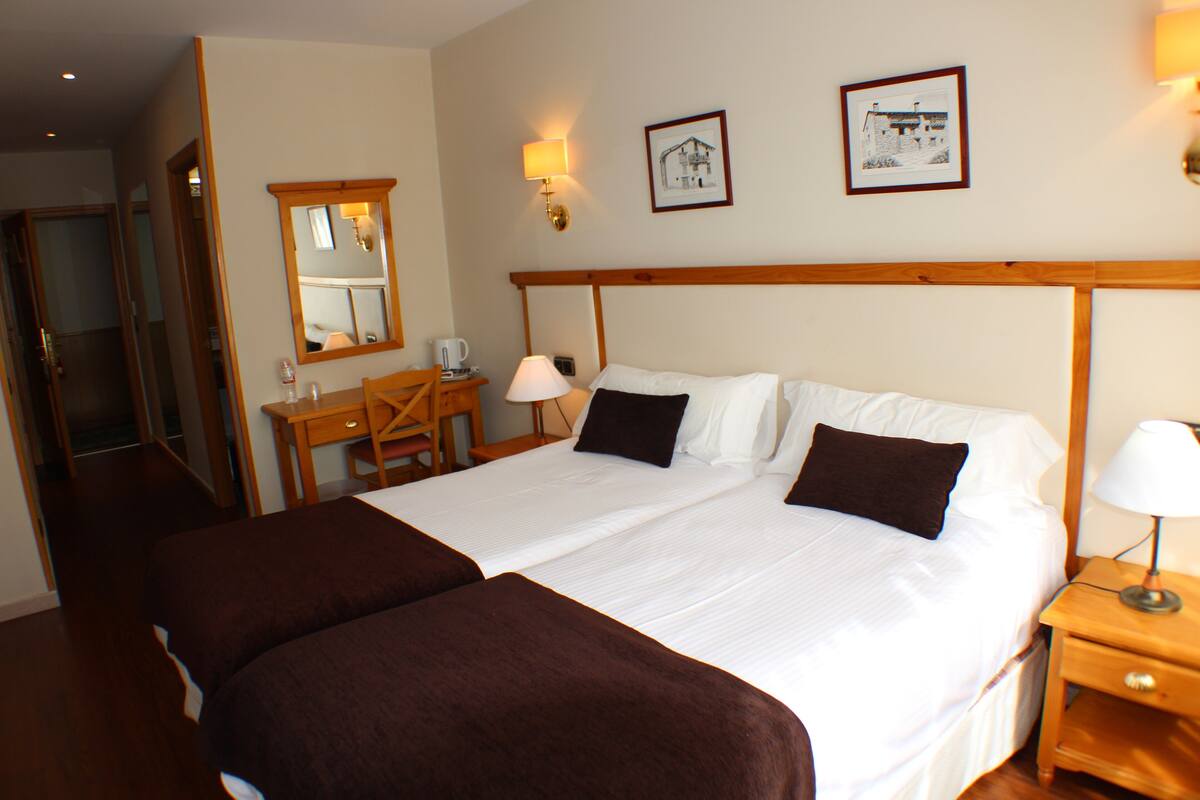 Une chambre d’hôtel avec un grand lit, un bureau avec une chaise, un miroir et deux tableaux encadrés au mur.