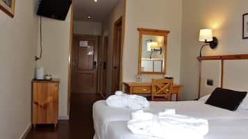 Habitación de hotel con dos camas, un escritorio de madera, un espejo, un televisor montado en la pared y un mueble pequeño.