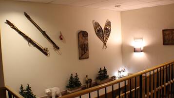 Una escalera con barandilla de madera y una pared decorada con esquíes, una placa de madera, una luz empotrada y pequeños abetos navideños.