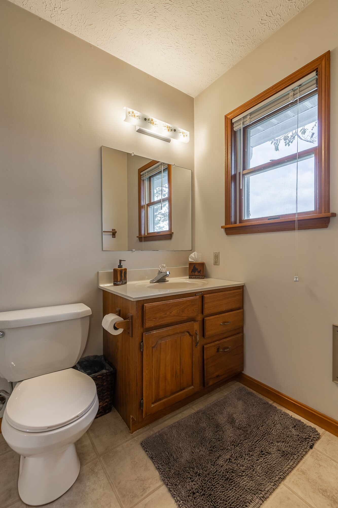 Ein Badezimmer mit Toilette, Holzwaschbecken, Spiegel und einem Fenster mit Jalousien.