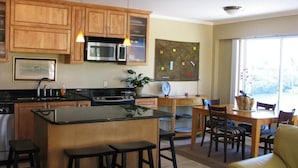 A kitchen with wooden cabinets, a central island with stools, a dining area with a table and chairs, and a large window providing natural light. - 2 Incredible Waterfront Homes - One Low Price! (Marathon)