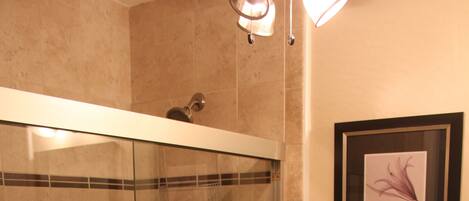 A bathroom with a glass-enclosed shower, a toilet, and two framed pictures on the wall.