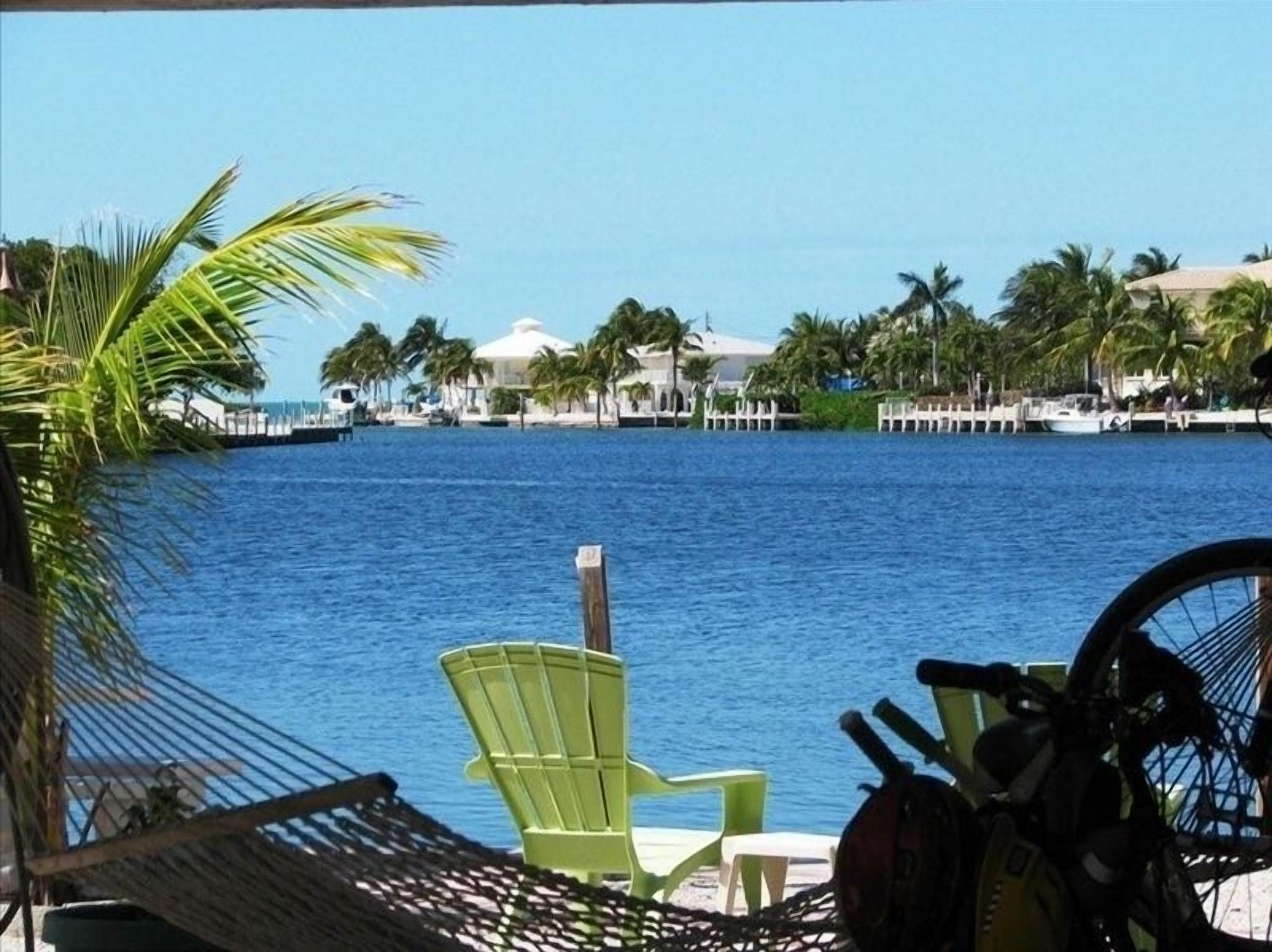 A view of a waterfront area with a hammock, a green chair, and a bicycle leaning against a railing.