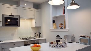 A modern kitchen with white cabinets, a built-in microwave, a gas stove, a kettle, a coffee maker, and a vintage radio. - The Old Stables At Westerton (Crieff)