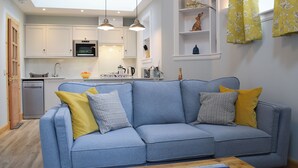 A modern living room with a blue sofa, a wooden coffee table, and a kitchen in the background. - The Old Stables At Westerton (Crieff)